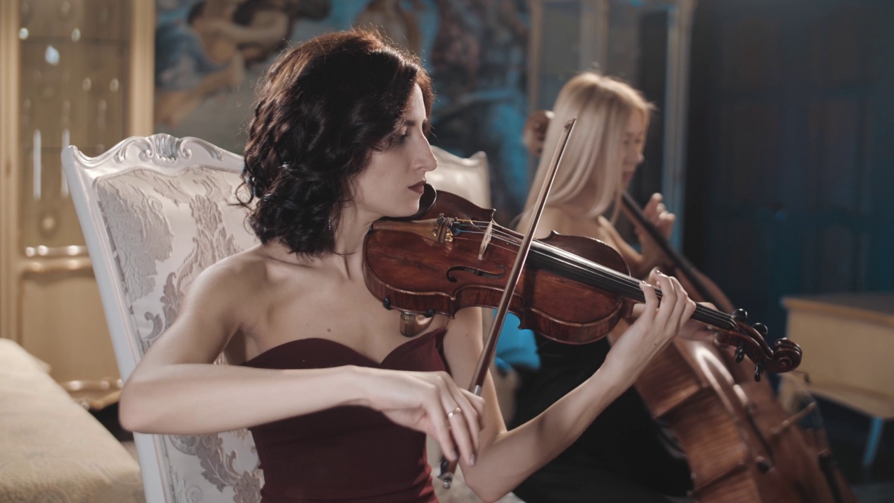 交响合唱。两个翩翩起舞的女孩拉着小提琴和大提琴。小提琴和大提琴。管弦乐队。视频素材