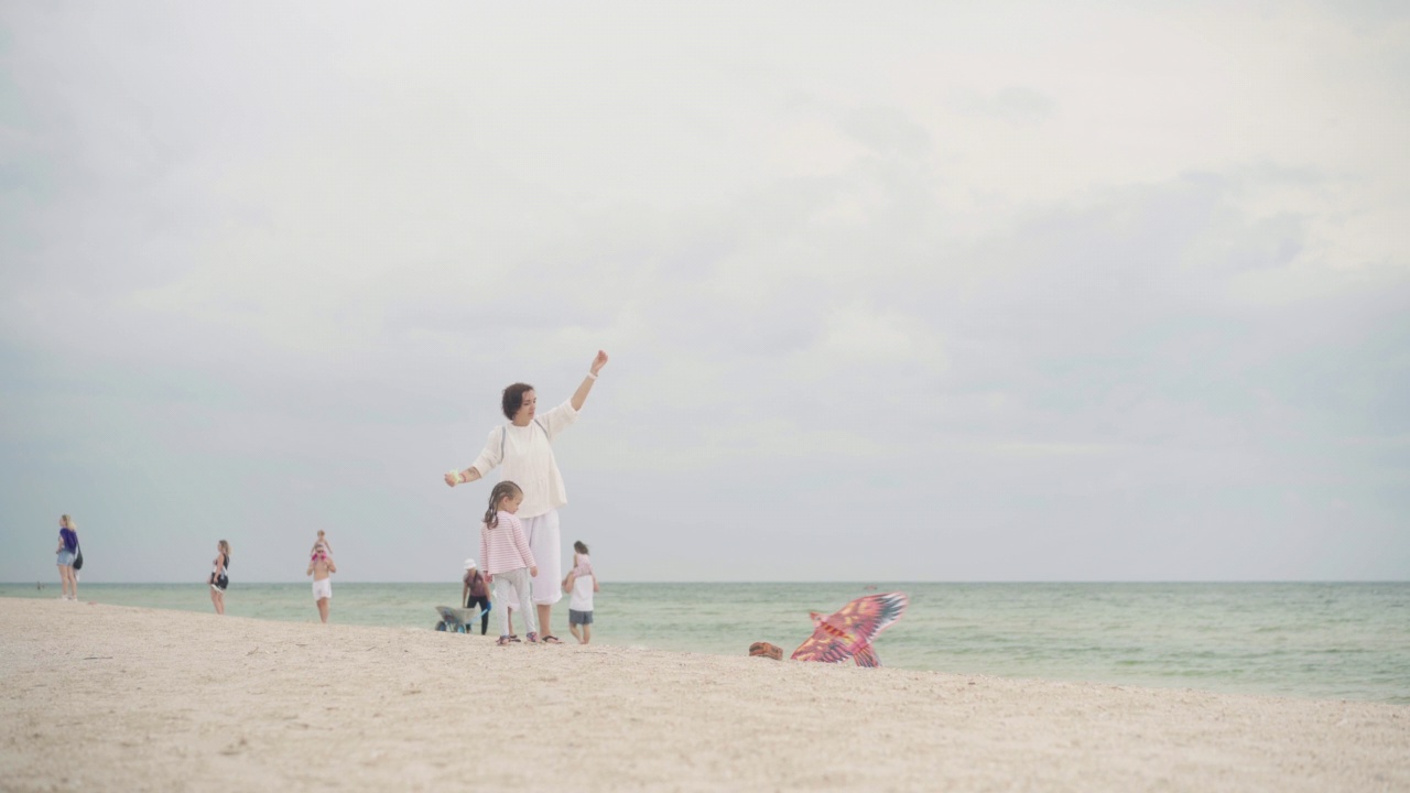母亲和小女儿在海滩上放风筝快乐的高加索家庭带着一个孩子在海滩上玩暑假视频素材