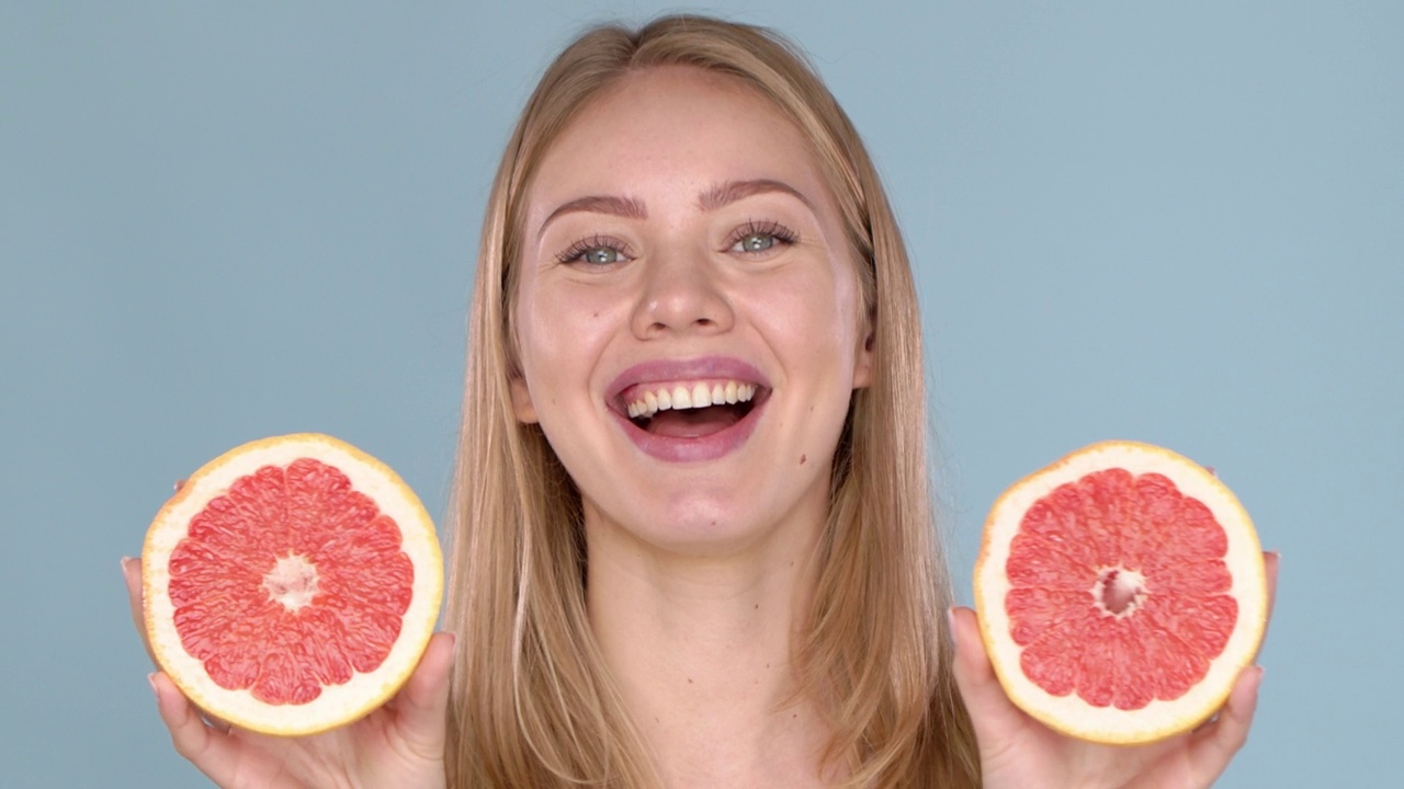 慢动作视频一个美丽的快乐微笑的年轻金发女人与葡萄柚一半视频下载