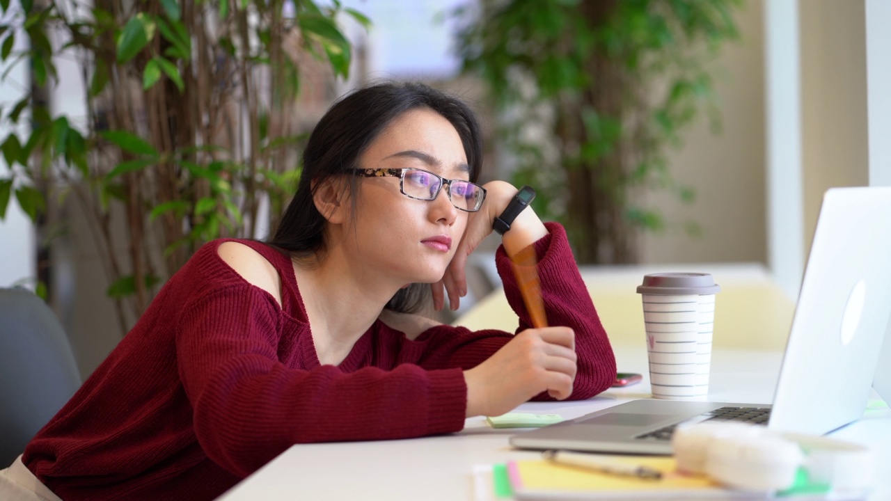 疲惫无聊的亚洲学生女孩在图书馆学习时戴着耳机在笔记本电脑上上网视频素材