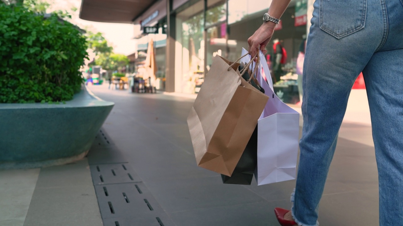 年轻的亚洲妇女走在购物区与许多袋子在手中。视频下载