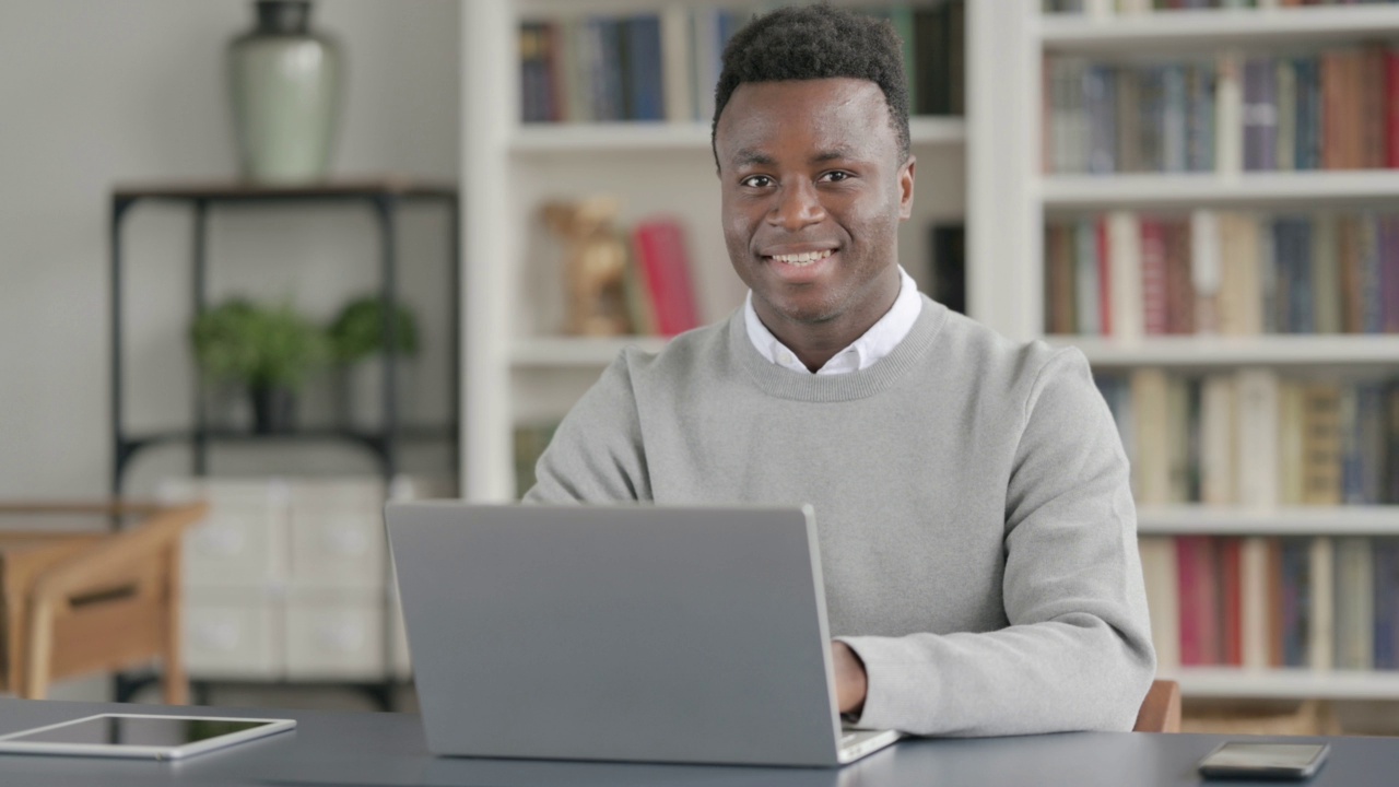 非洲男子在图书馆使用笔记本电脑时对着相机微笑视频素材