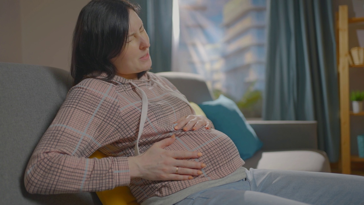 一位孕妇坐在沙发上，近距离地体验着不适视频下载