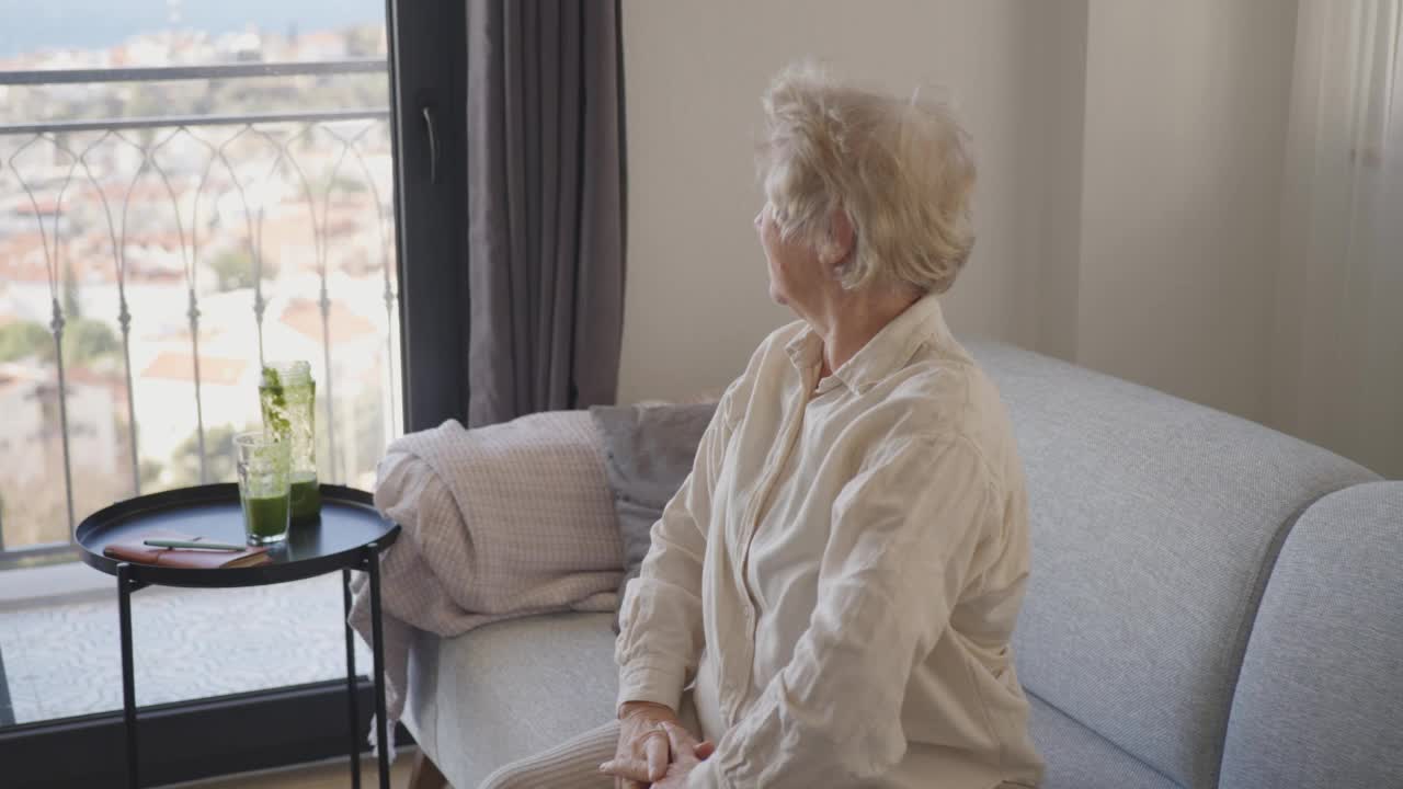 微笑的老妇人放松在客厅的沙发上。视频素材