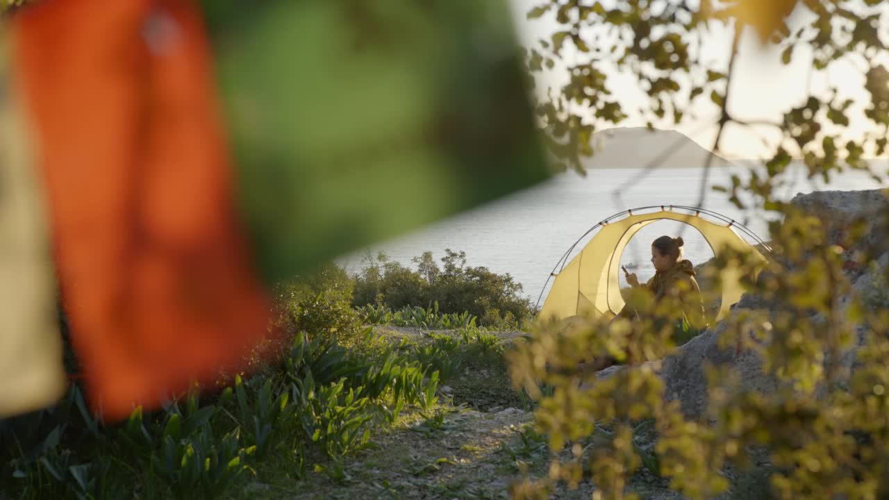 一名女徒步旅行者坐在旅游营地的帐篷里使用手机。视频素材