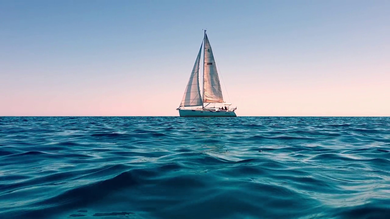 缩小和低角度的海平面小游艇航行在平静的开阔海面日落。慢动作视频素材