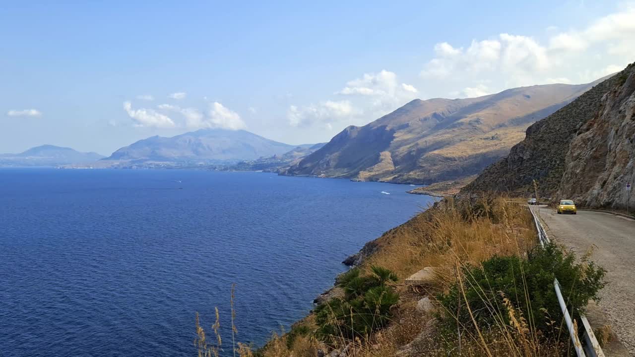 慢动作全景平移西西里岛Riserva dello Zingaro自然保护区在西西里岛与黄色汽车在沿海道路。意大利视频素材