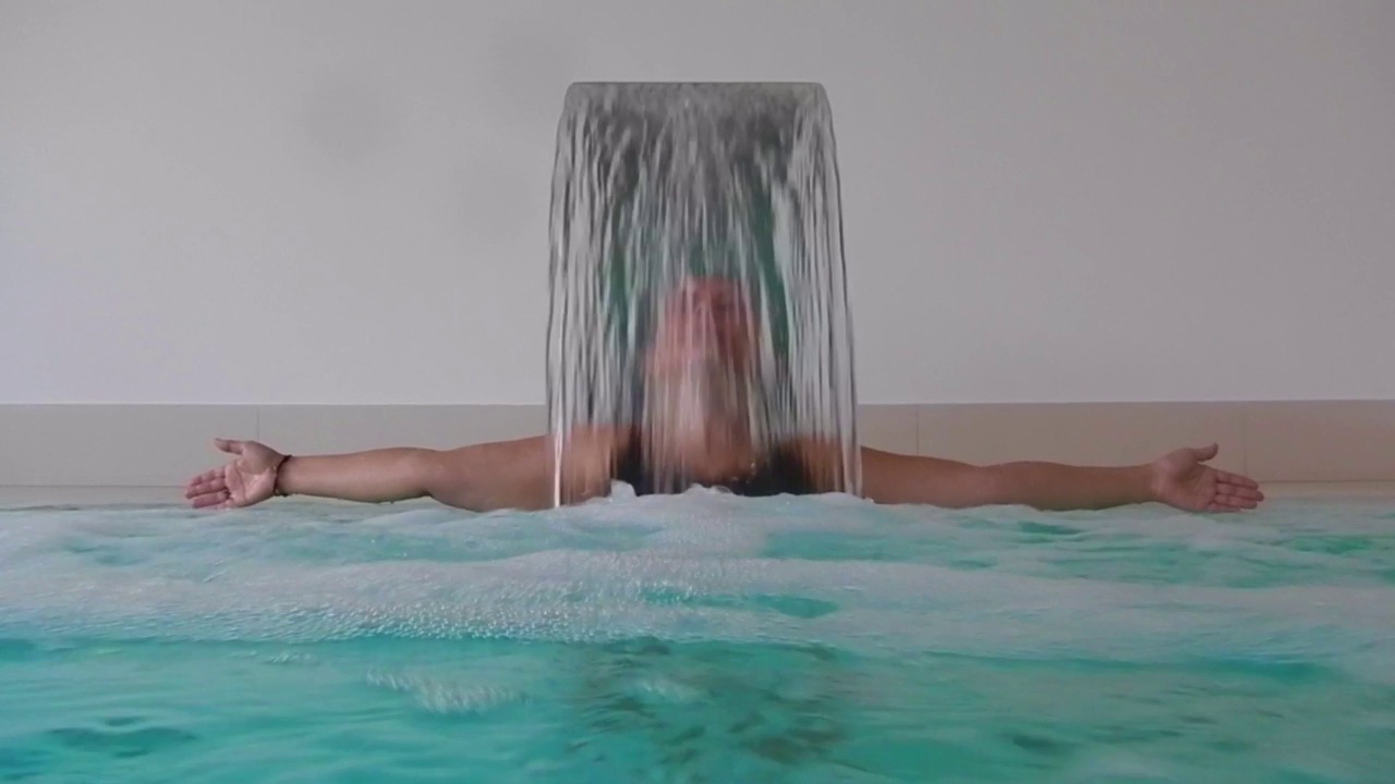 女人在水疗按摩池与下降的水在游泳池与手臂伸展视频下载