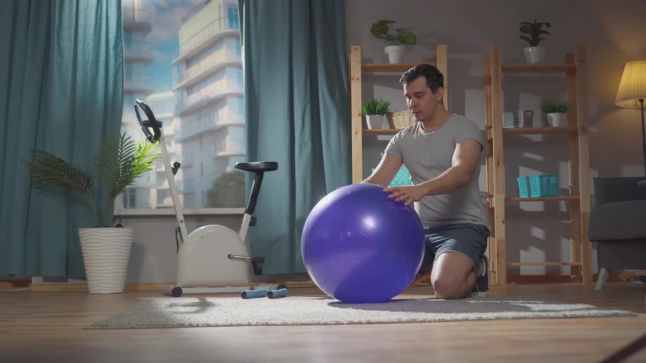一名男子在家里客厅的健身球上健身课时感到剧烈疼痛视频下载