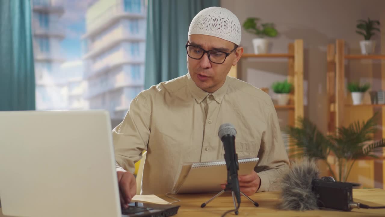 一名戴着眼镜、头戴无边便帽的穆斯林肖像男子坐在客厅的麦克风前录制播客视频下载