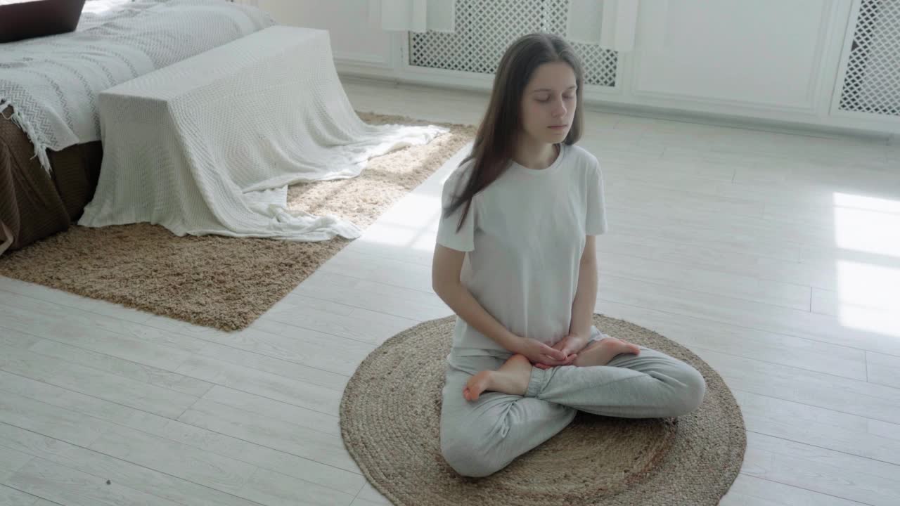 一个年轻漂亮的女人坐在明亮的房间里，铺着黄麻地毯，闭着眼睛冥想视频素材