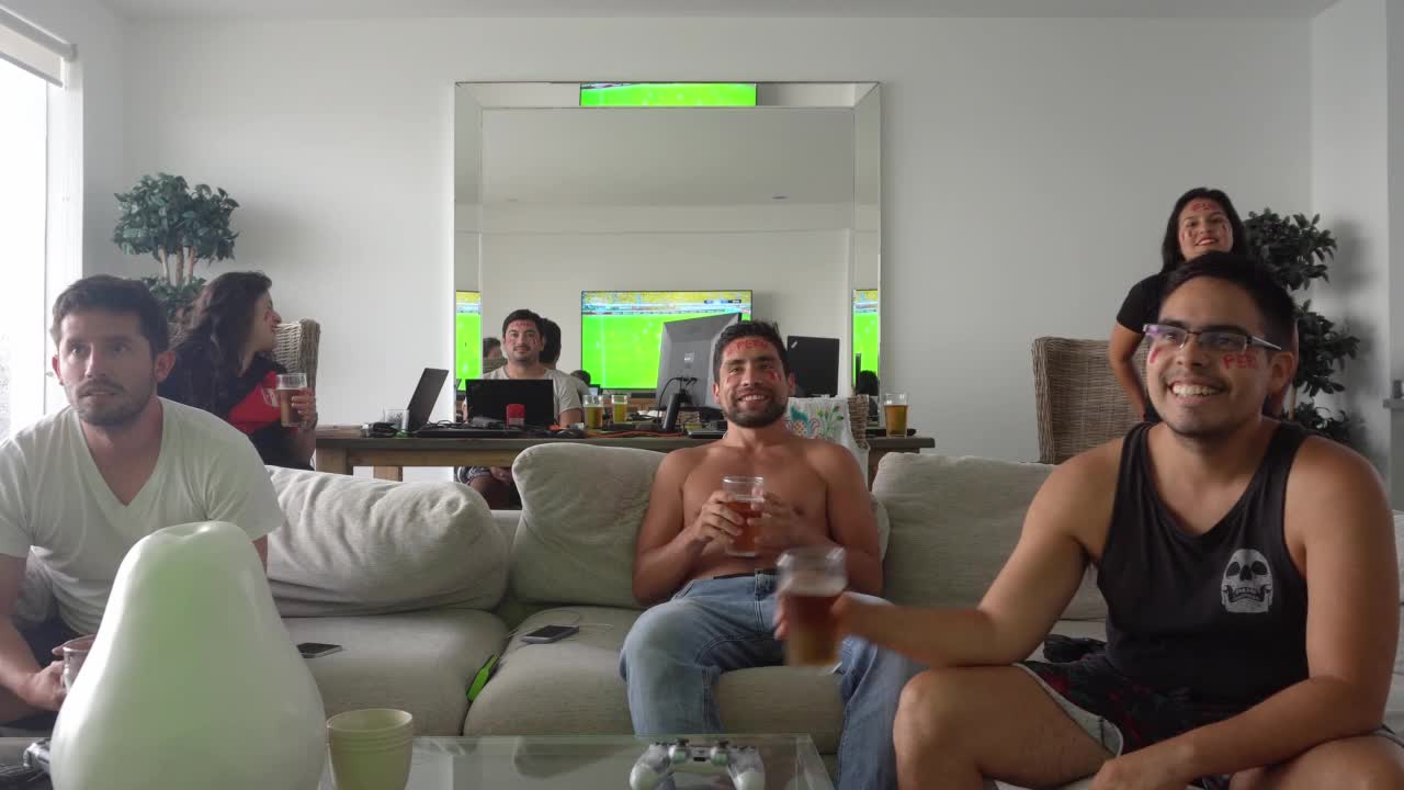 几个男性和女性朋友在客厅里看他们最喜欢的球队的足球比赛，喝着啤酒，在海滩别墅里笑着。4k时间间隔视频下载