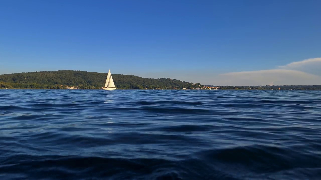 慢动作和低角度的看法小船航行在平静的开放的湖面马乔里湖在意大利。的放大视频素材