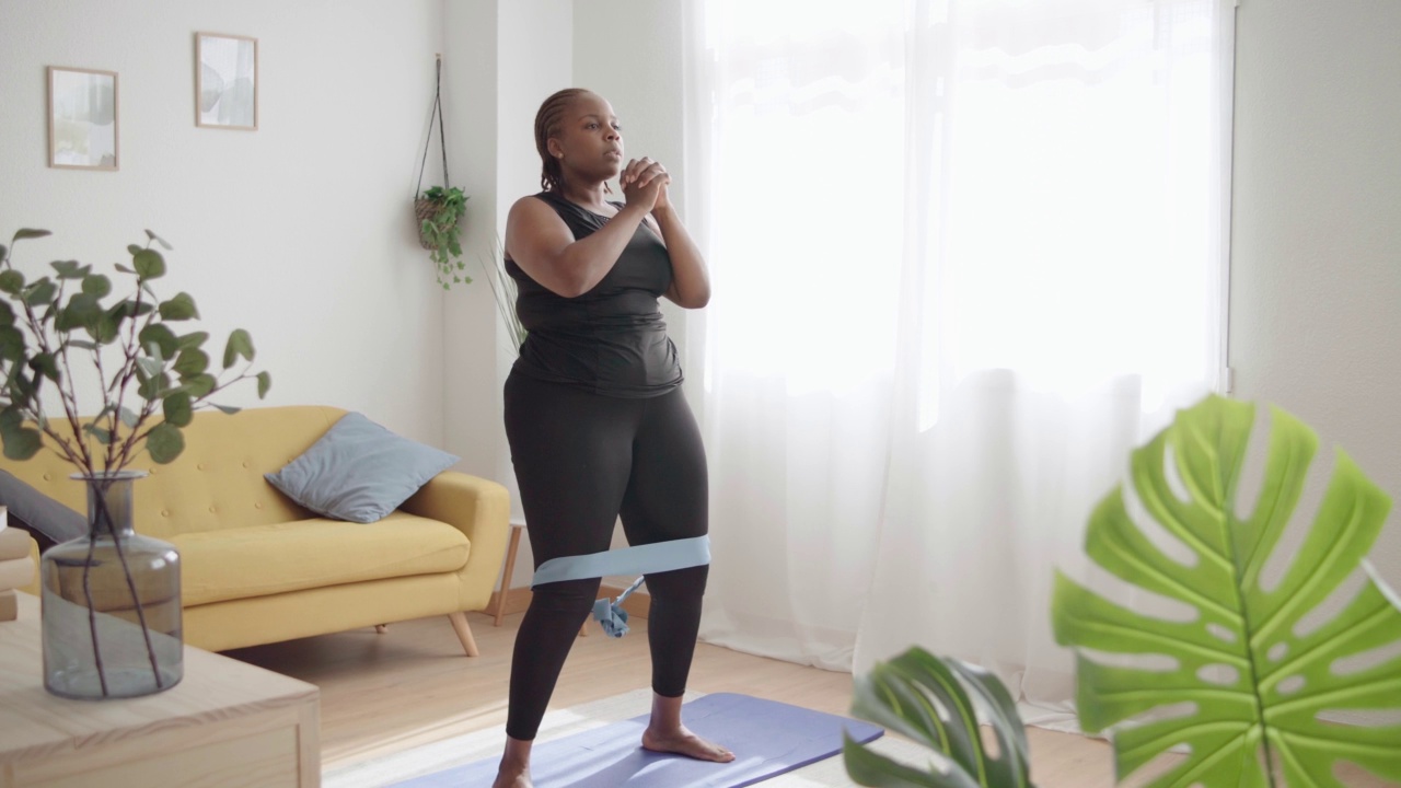 健身妇女在家里用阻力带做下蹲运动。视频下载