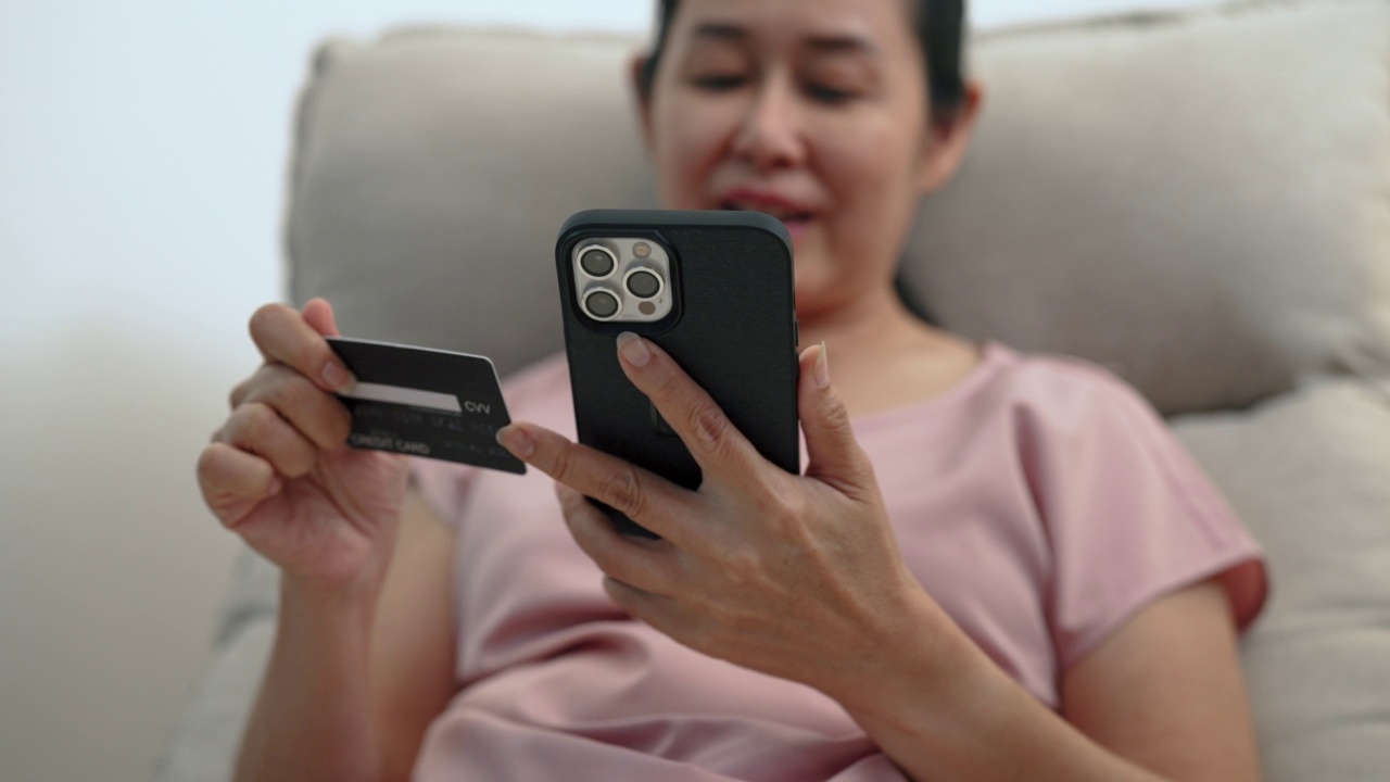 高级亚洲妇女看信用卡添加到支付细节。视频下载