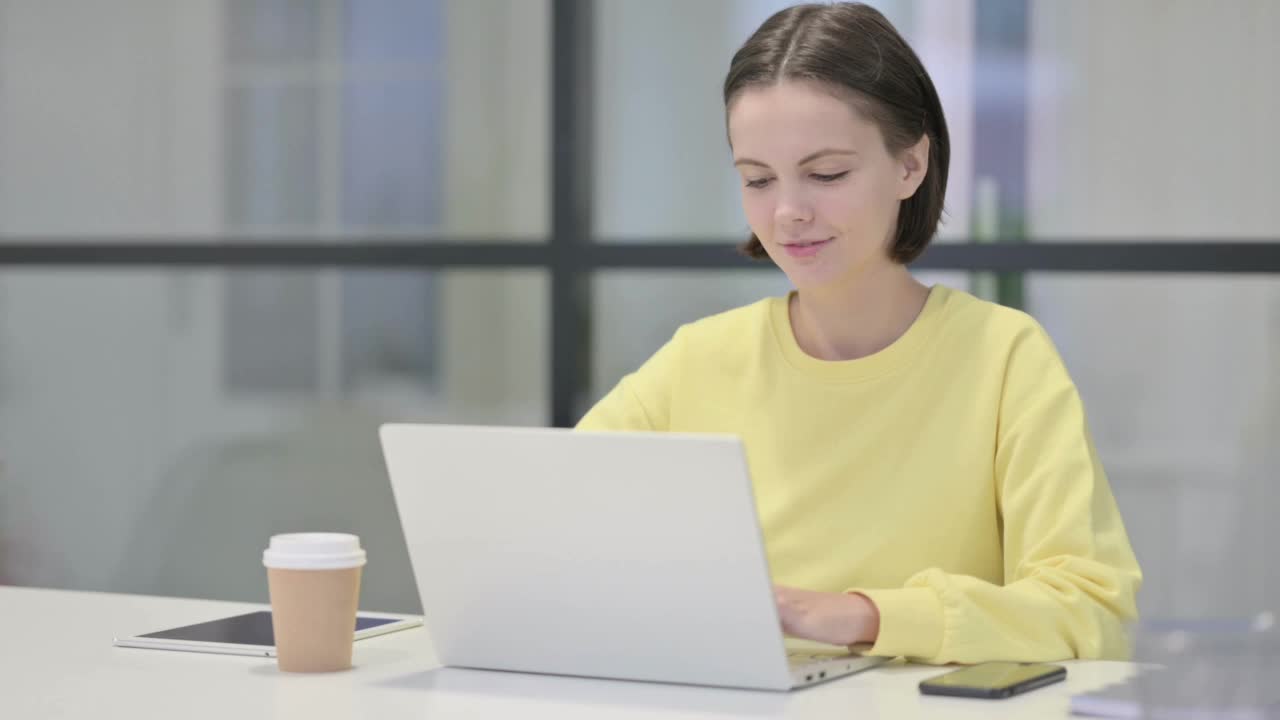 年轻女子在办公室使用笔记本电脑时对着相机微笑视频素材