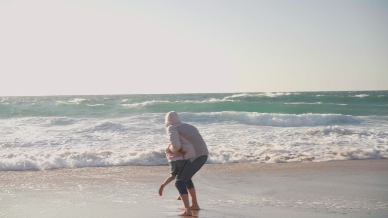 母亲和孩子在春天的海滩上玩海洋，穿着暖和的衣服，赤脚手持视频效果视频素材
