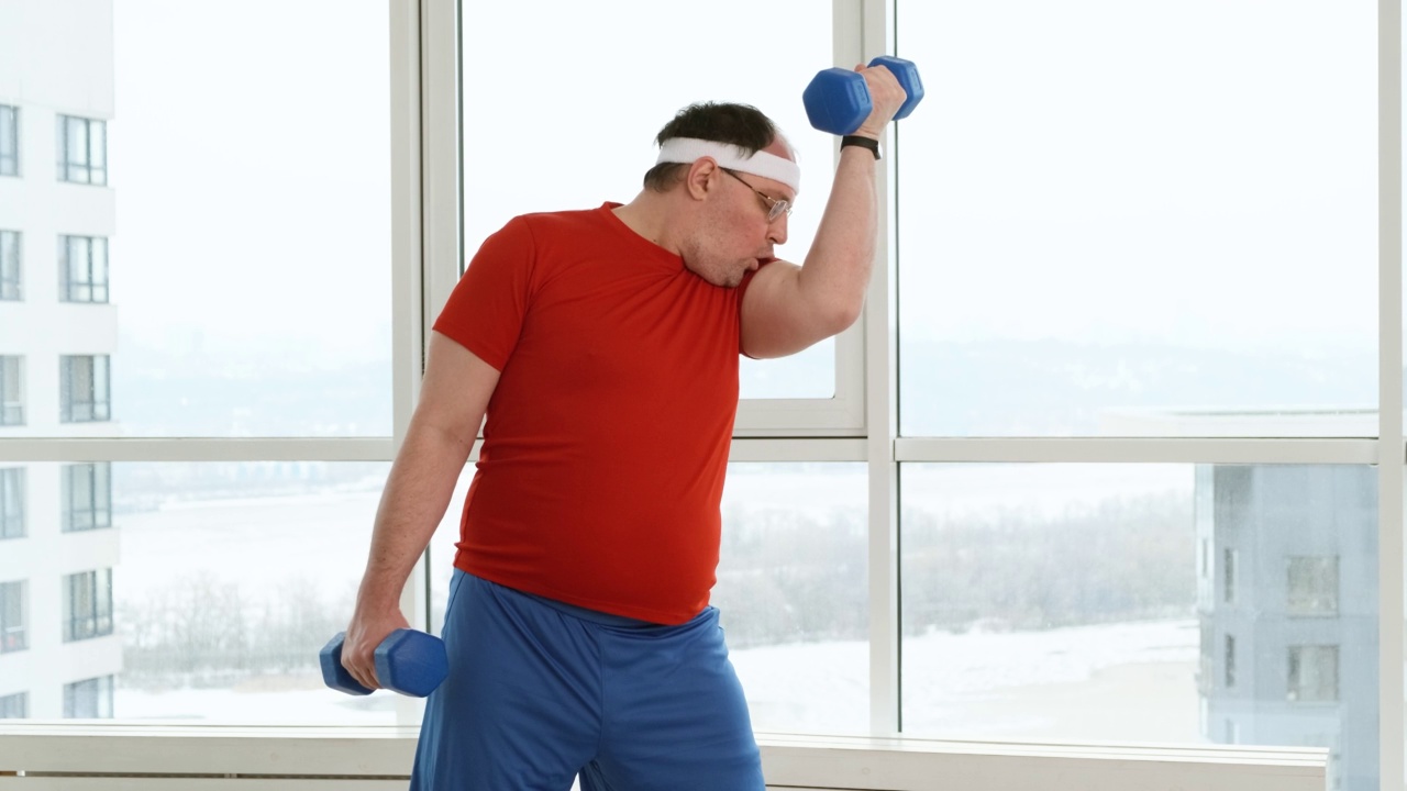胖运动员在家里或健身房锻炼时，以滑稽的姿势站着做运动视频下载