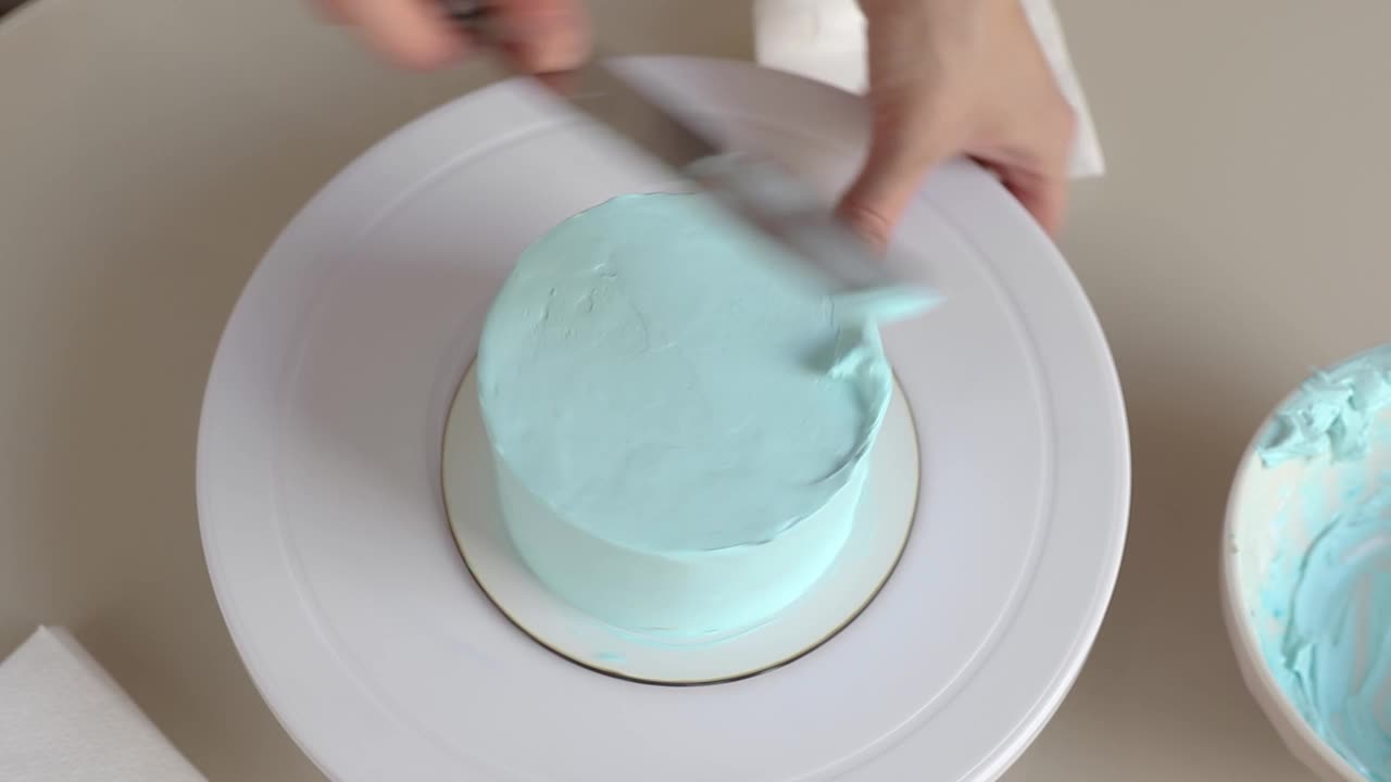 糖果师用烹饪抹刀近距离地将蓝色奶油涂在圆形蛋糕上视频下载