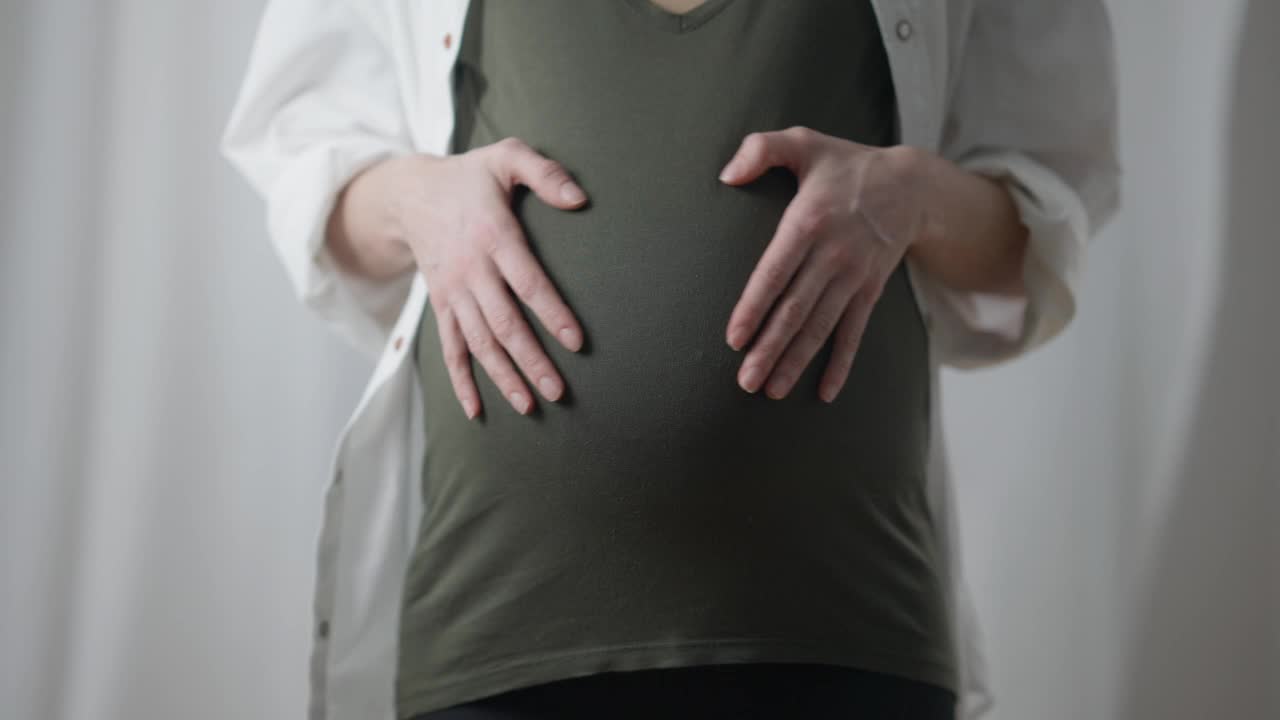 孕妇站在室内，腹部呈心形。无法辨认的快乐的白人孕妇享受怀孕。视频素材