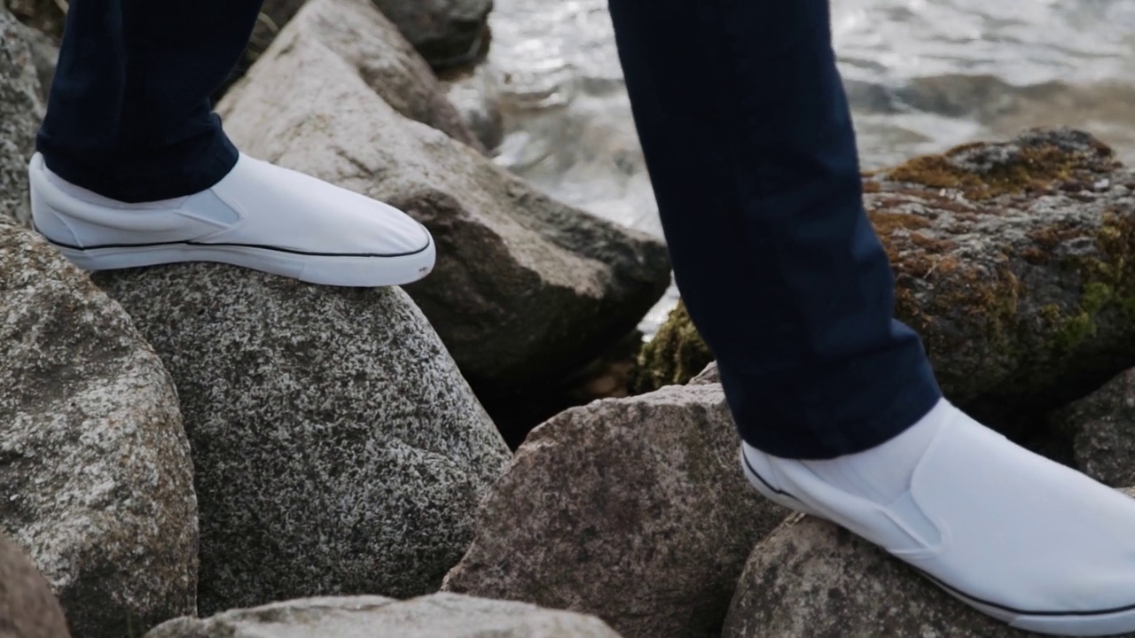 腿部特写，穿着白色运动鞋的男人，走在河边的石头上，海边视频素材