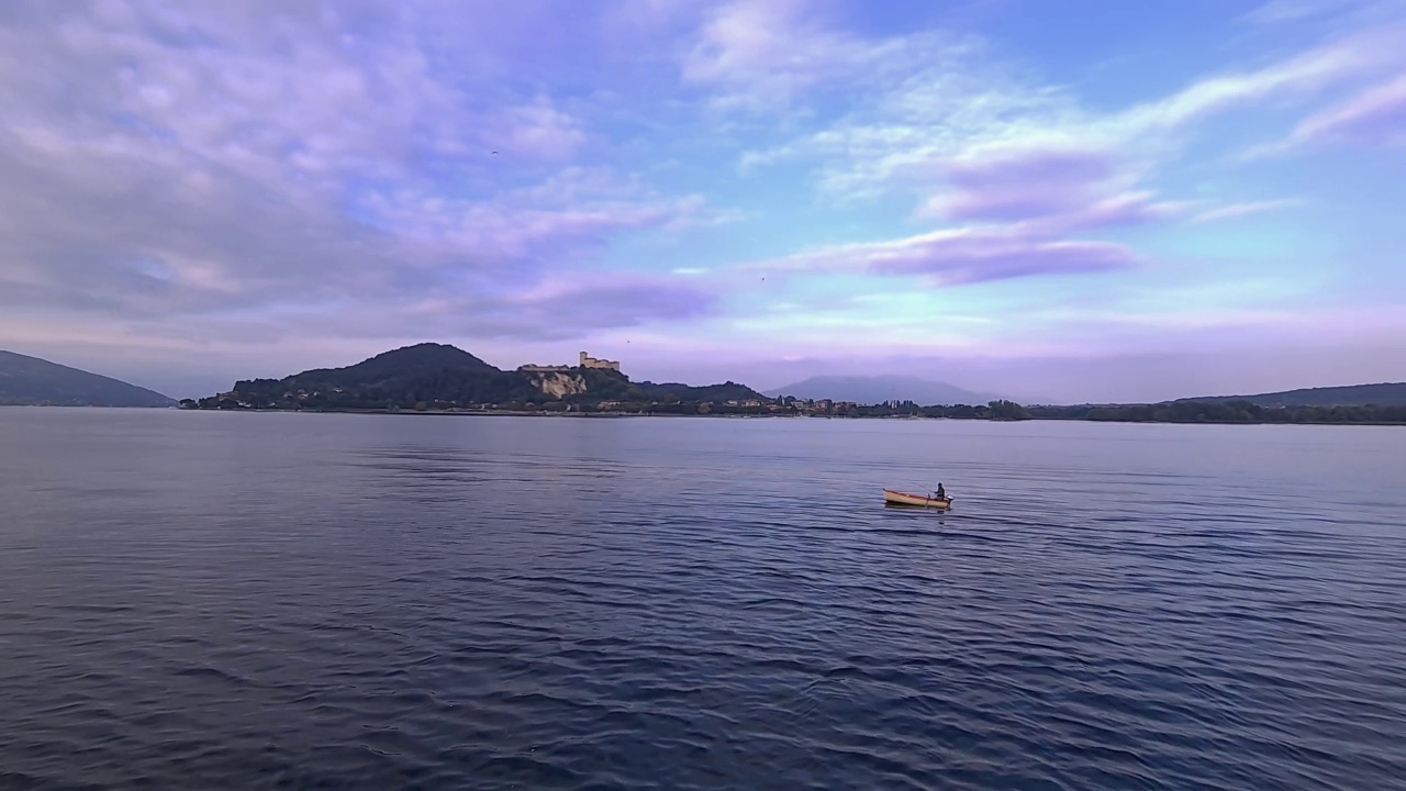小渔船与渔民划船在平静的湖面在意大利与安杰拉城堡背景的湖面广角视图视频素材