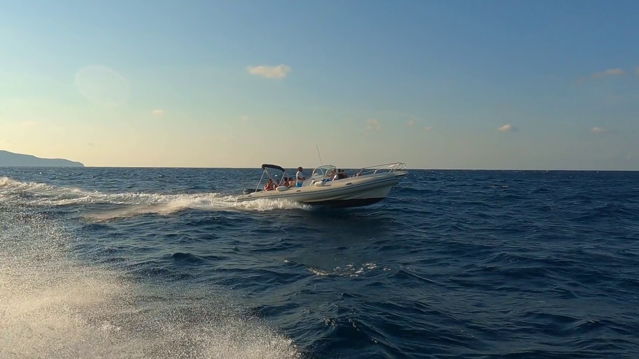 从其他高速航行的船只上看到的有人在海水中航行的小橡皮艇的低角度海平面视图。慢动作视频素材