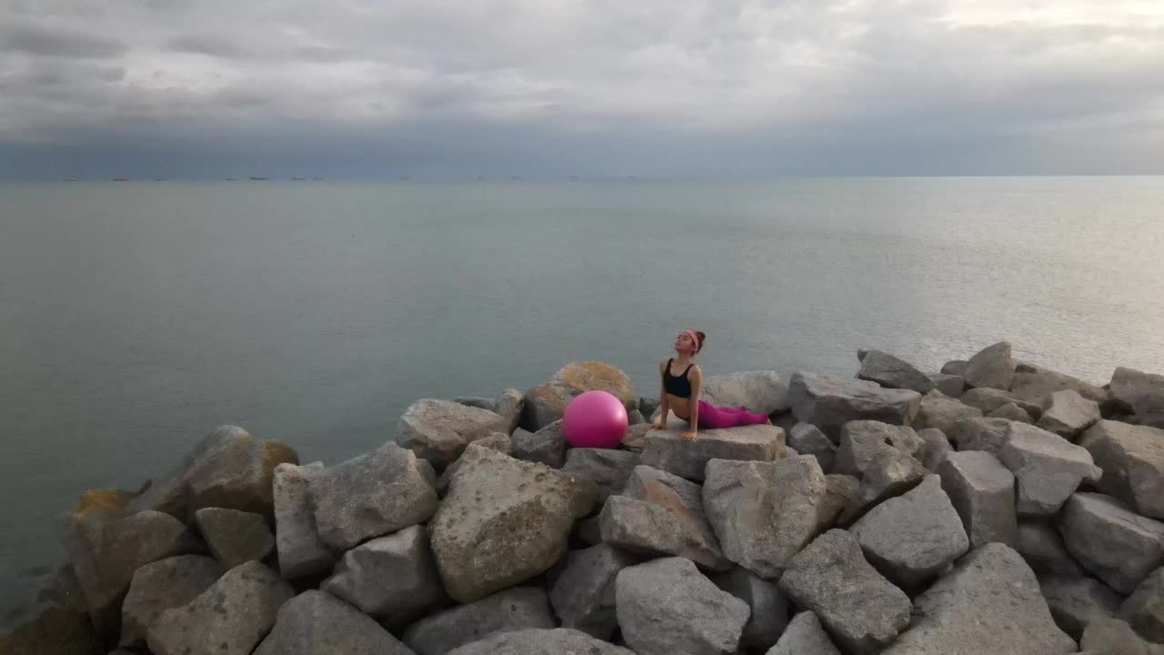 一名亚洲女子在岩石斜坡上练习瑜伽。视频下载