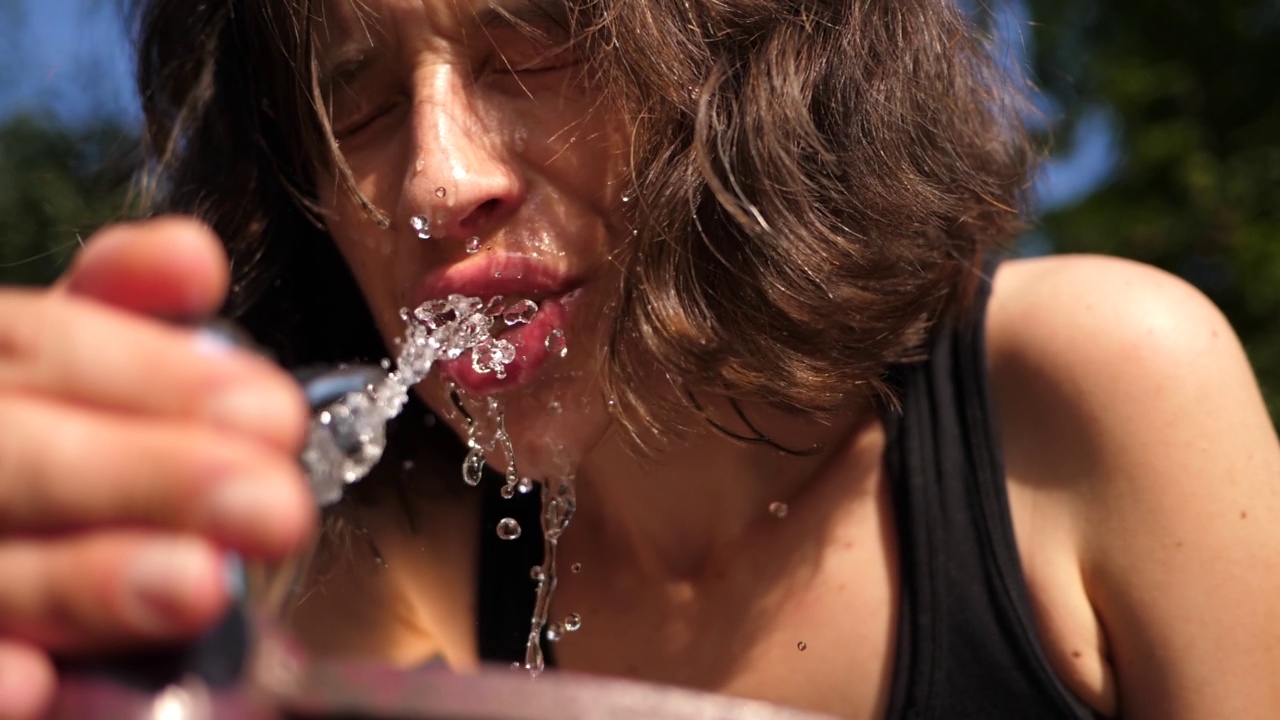 女人喝水从饮水机在炎热的夏天在一个城市特写脸在慢动作视频下载