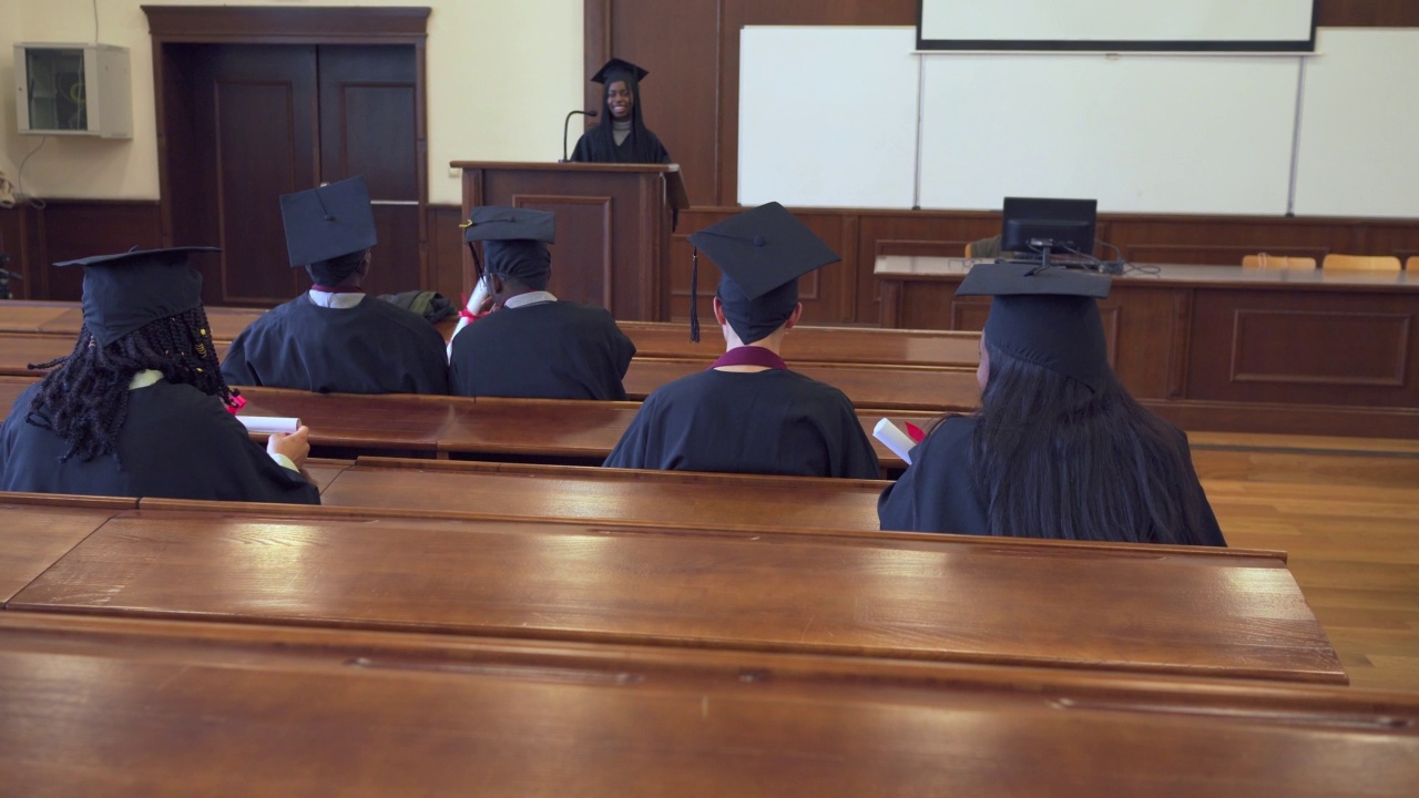 毕业生穿着毕业礼服坐在演讲厅里的背影视频素材