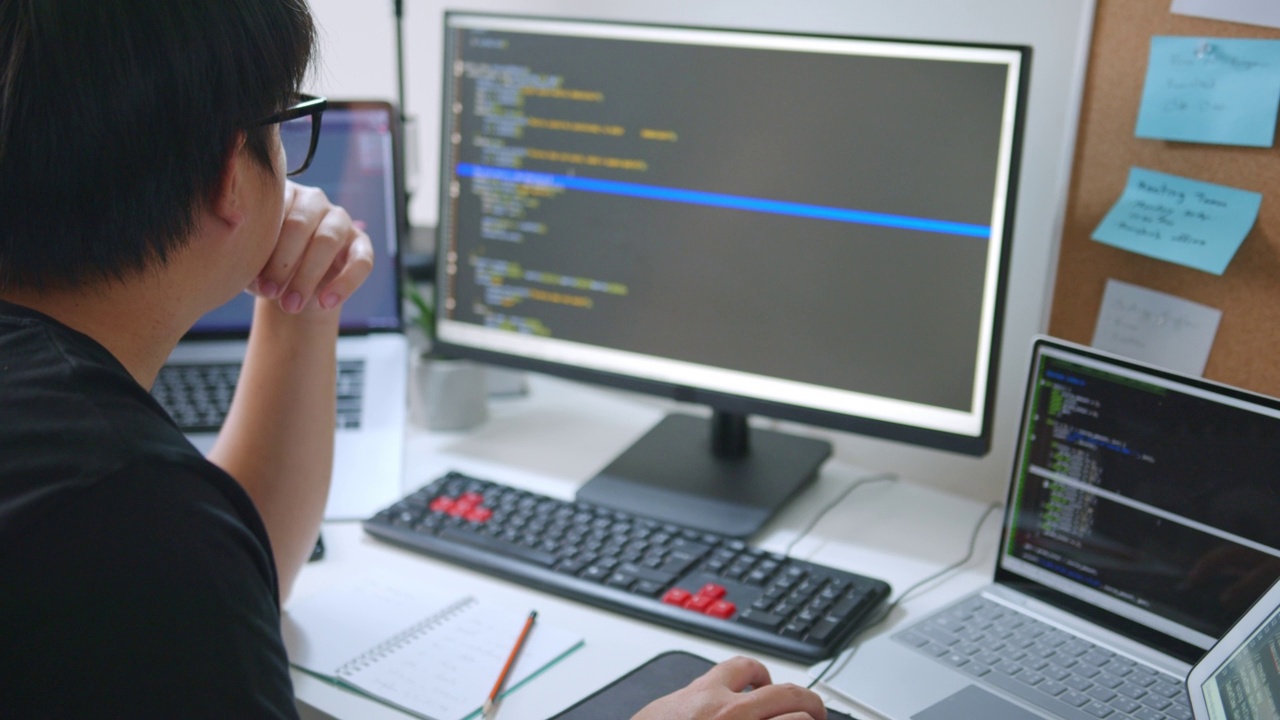年轻的亚洲人，开发程序员，软件工程师，IT支持，戴着眼镜在电脑上检查窃听系统中的代码。后视图视频素材