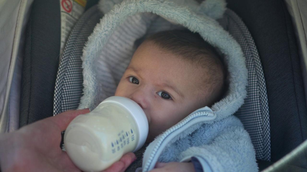 婴儿车里的婴儿从奶瓶里吮吸牛奶。一个新生儿在走路时吃东西的特写镜头。视频素材