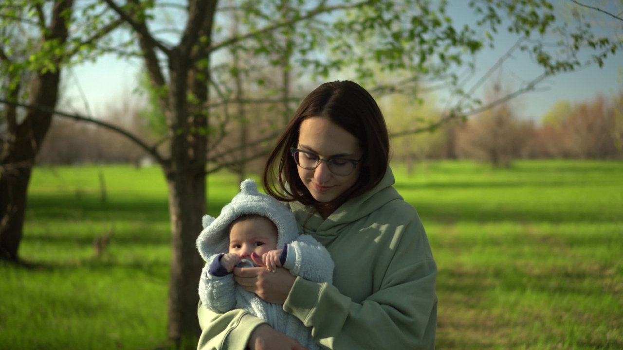 一位年轻的母亲在大自然中带着婴儿散步。一个戴眼镜的女孩怀里抱着一个孩子。特写镜头。视频素材