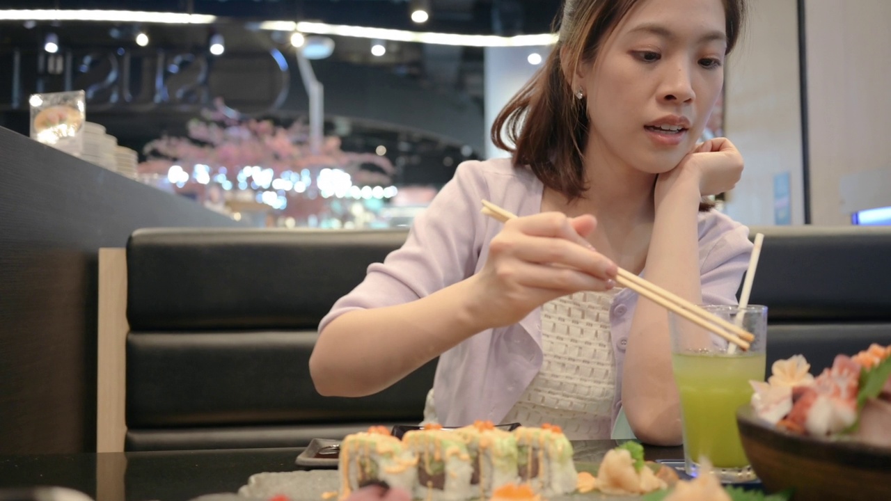 亚洲泰国华人商业女性穿着现代的衣服，拿着筷子吃鳄梨寿司和新鲜的沙士米高档集在泰国曼谷的餐厅视频下载