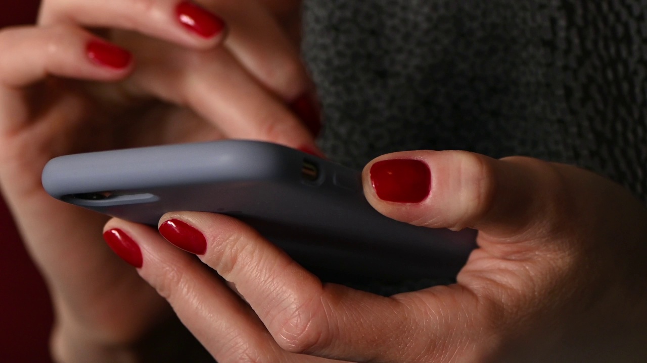 女人的手与红色的指甲拿着手机和短信视频素材