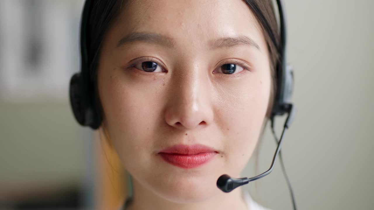 年轻的亚洲女人的特写，呼叫中心，客户服务戴着耳机和微笑。看看相机视频素材