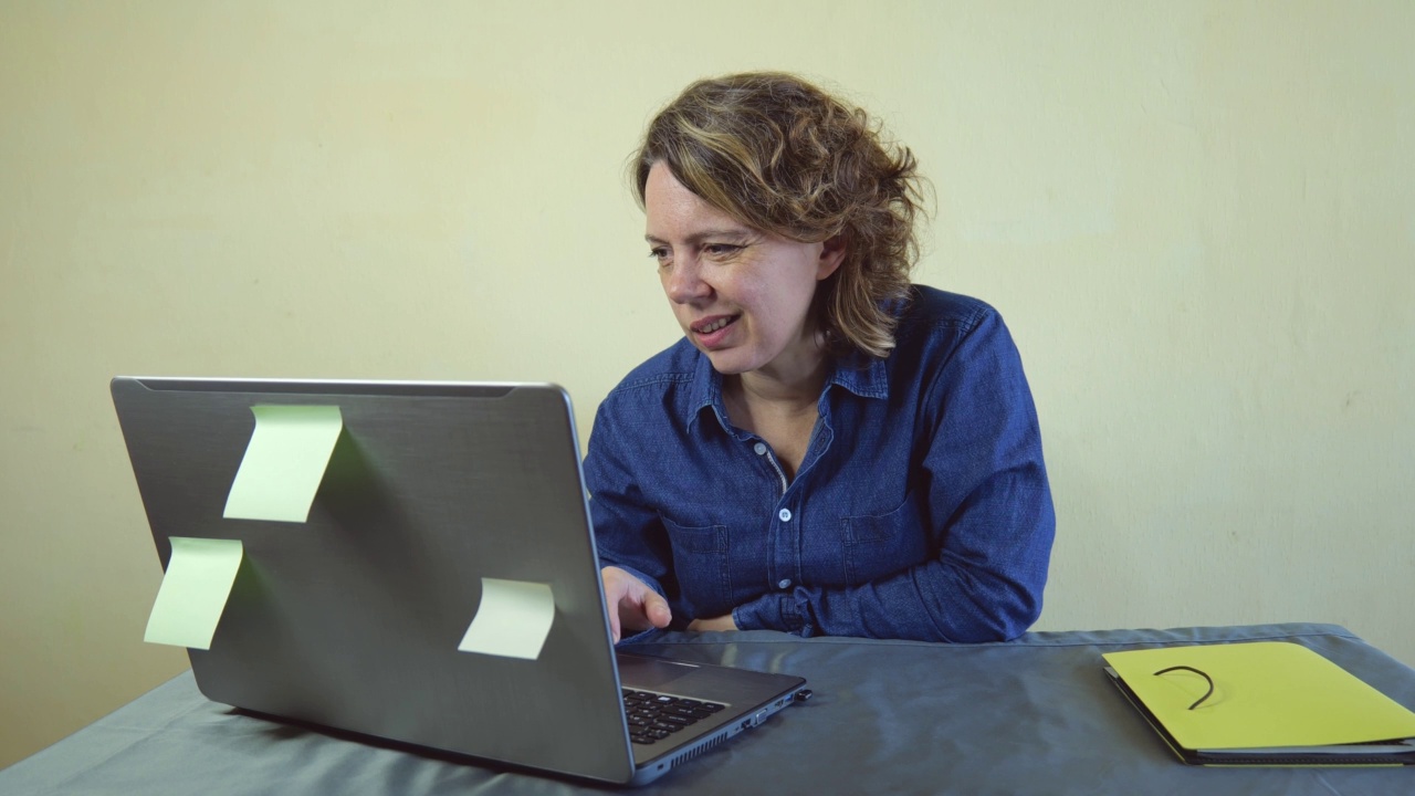 一位穿着牛仔衬衫的40岁妇女在笔记本电脑前工作。女性成人自由职业者视频素材
