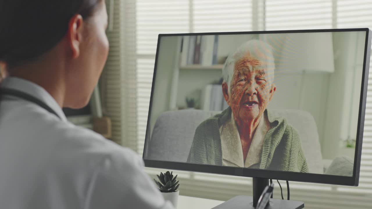 女亚洲医生视频电话与亚洲老年妇女灰白头发80-90年代，远程医疗远程保健的概念视频素材
