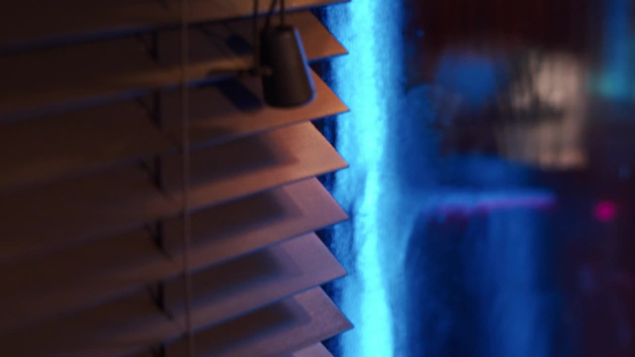 黑暗的客厅被蓝色和粉色的led灯照亮。看着百叶窗视频素材