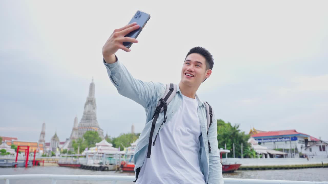 一名亚洲男子背包客用手机拍摄佛寺。年轻的男性游客独自在城市的街道上旅行，用手机记录视频日志在泰国度假旅行。视频下载