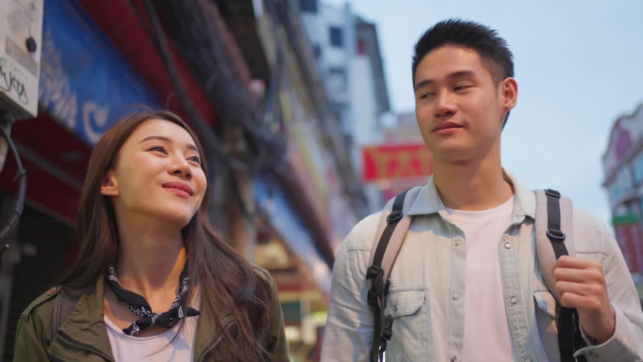 亚洲活跃的年轻夫妇晚上在城市旅行蜜月旅行。迷人的新婚男人和女人背包游客走在街上享受花时间约会情人节假期在一起视频素材