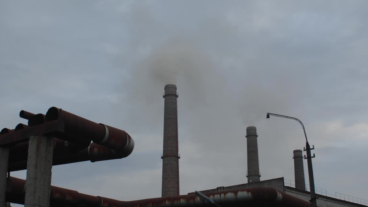 在多云的天空下，三个热电厂烟囱的跟踪镜头。烟出来。全球变暖、环境灾难和使用不可持续燃料的概念视频素材