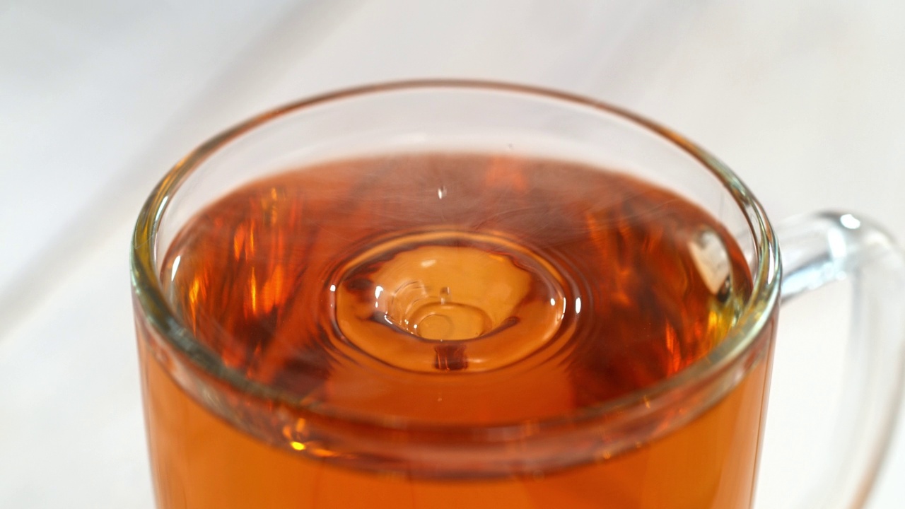 在明亮的背景下，茶滴在透明杯上溅起水花，荡起涟漪视频下载