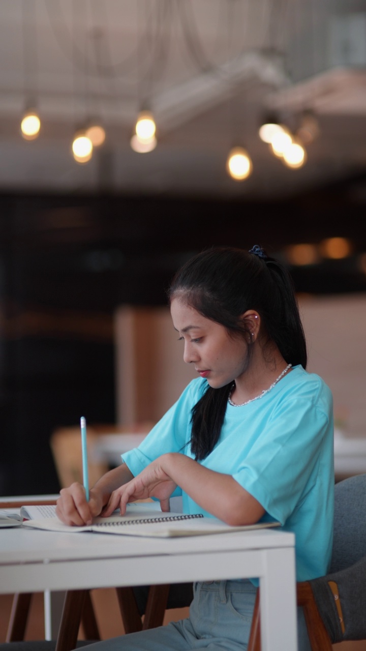 亚洲女学生在笔记本电脑上写，同时使用笔记本电脑在学校图书馆学习做作业视频下载