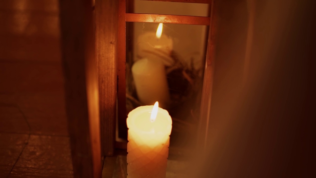 白蜡蜡烛在木桌旁燃烧，火焰在玻璃中反射视频素材