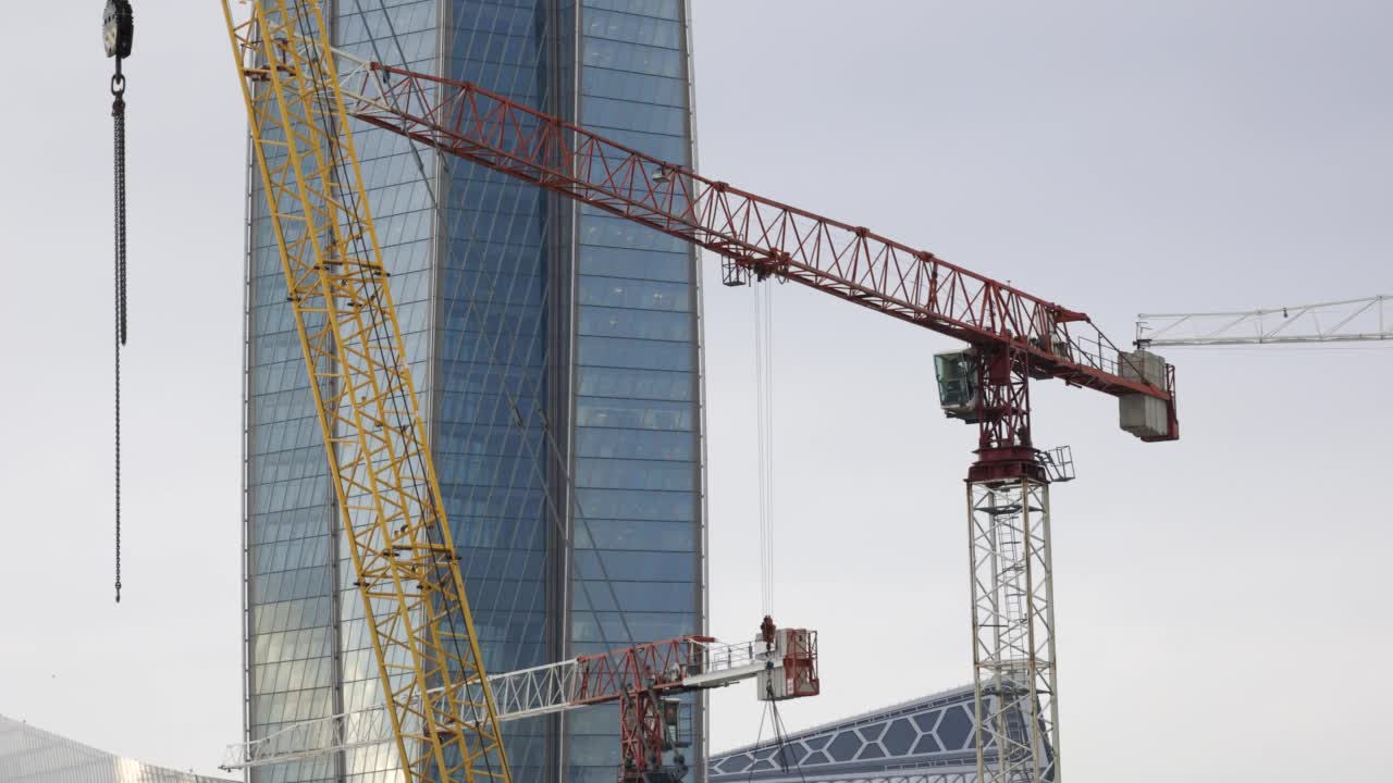 高架起重机在一个玻璃建筑塔的工地上工作视频素材