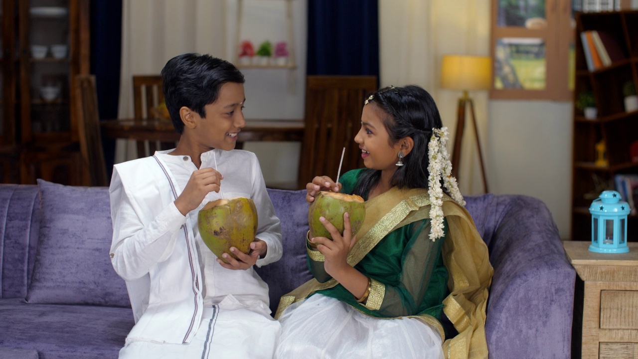 一个快乐的印度兄弟姐妹喝嫩椰子-夏天，清爽的饮料，传统的南印度服饰视频素材