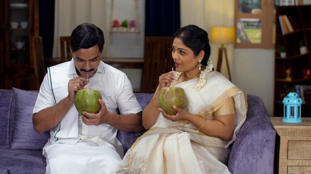 一对幸福的南印度夫妇穿着民族服装，用吸管喝着嫩椰汁——清爽的饮料，自然视频素材