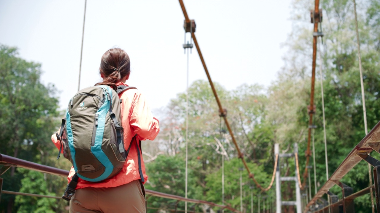 一名年轻女子在森林中穿越一座木制吊桥视频素材