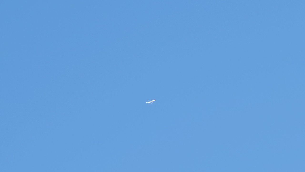 远处的喷气式客机在晴朗的蓝天上高高地飞行，留下白色的烟雾和尾迹。航空运输的概念视频素材